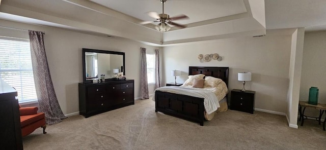 carpeted bedroom with ceiling fan, a raised ceiling, and multiple windows