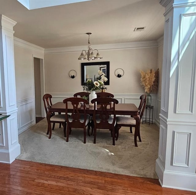 dining area with a notable chandelier, wood-type flooring, ornamental molding, and ornate columns