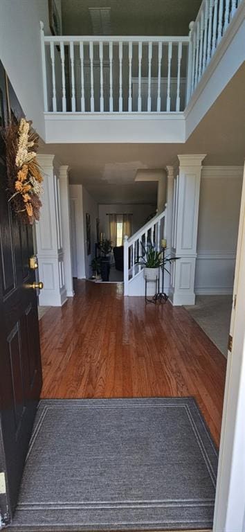 entrance foyer with ornamental molding, a towering ceiling, wood-type flooring, and decorative columns