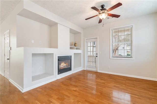 unfurnished living room featuring ceiling fan, hardwood / wood-style floors, a textured ceiling, and built in shelves