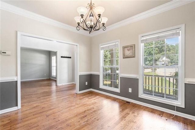 spare room featuring an inviting chandelier, hardwood / wood-style flooring, plenty of natural light, and ornamental molding