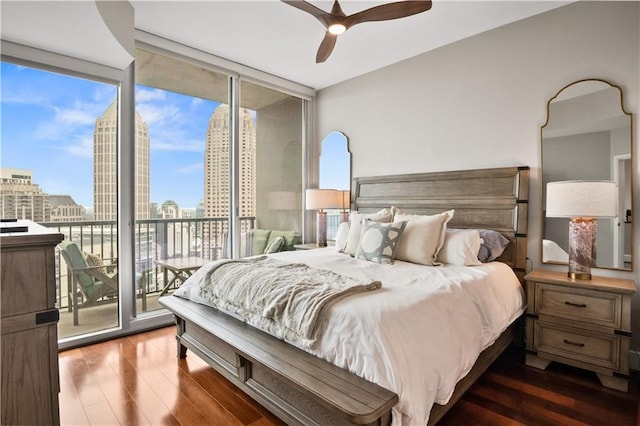 bedroom with access to exterior, a view of city, floor to ceiling windows, ceiling fan, and wood finished floors