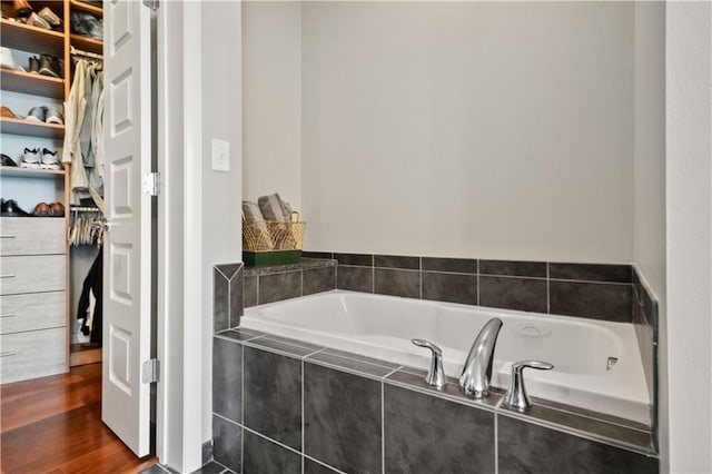 full bath with a walk in closet, a garden tub, and wood finished floors