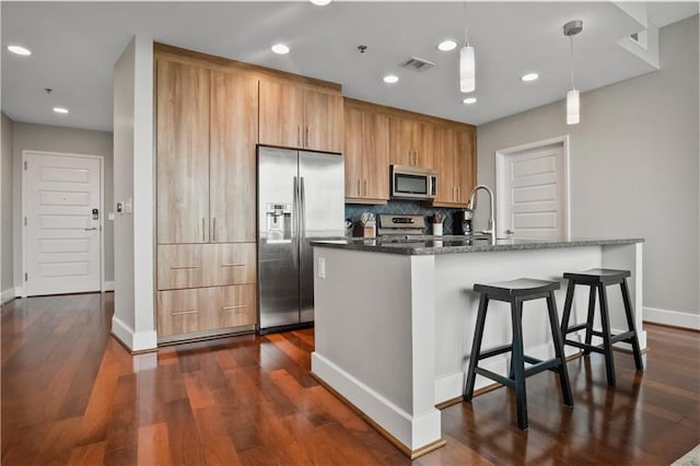 kitchen with tasteful backsplash, visible vents, an island with sink, appliances with stainless steel finishes, and dark wood-type flooring