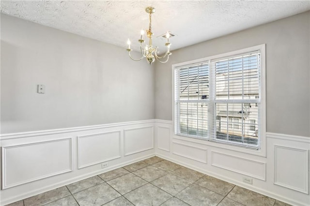 unfurnished room featuring a chandelier, a textured ceiling, and light tile patterned floors