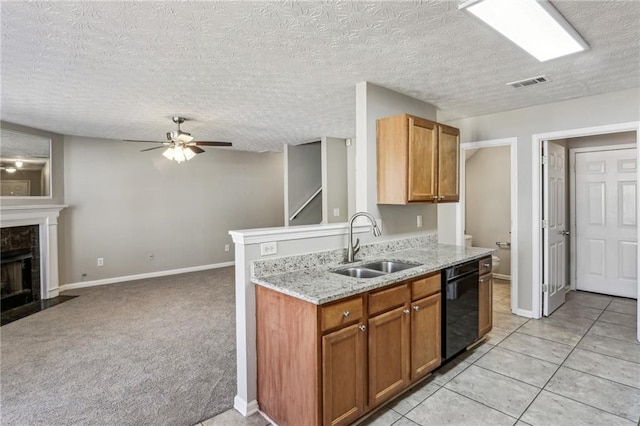 kitchen featuring sink, dishwasher, light stone countertops, a tiled fireplace, and light carpet