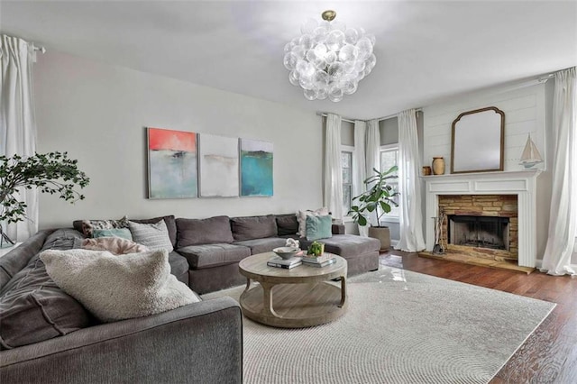living room featuring a stone fireplace, wood finished floors, and a notable chandelier