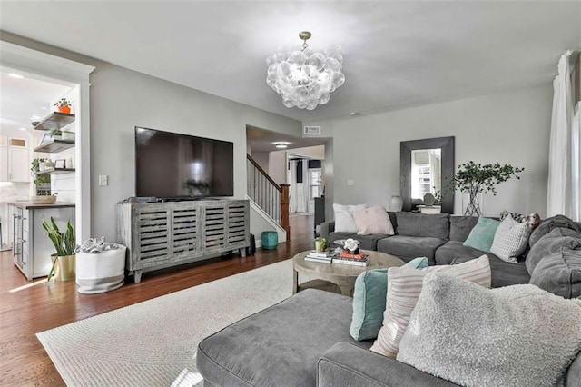 living area featuring a chandelier, wood finished floors, visible vents, and stairway