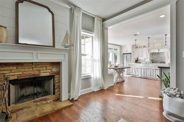 living area featuring wood finished floors, ornamental molding, baseboards, and a stone fireplace