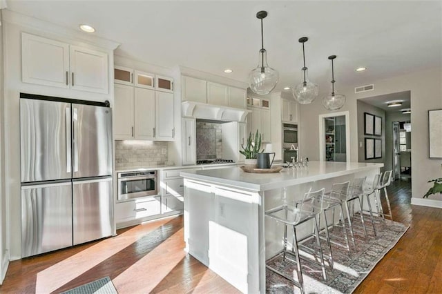 kitchen with white cabinets, stainless steel appliances, a center island with sink, visible vents, and premium range hood