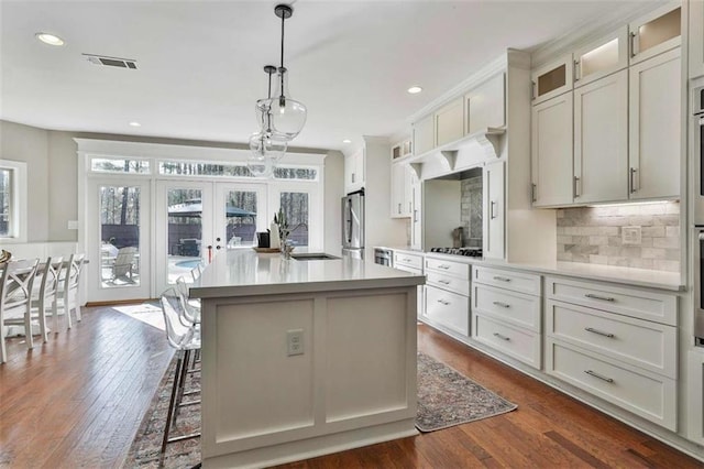 kitchen with a sink, a kitchen island with sink, french doors, dark wood-type flooring, and freestanding refrigerator