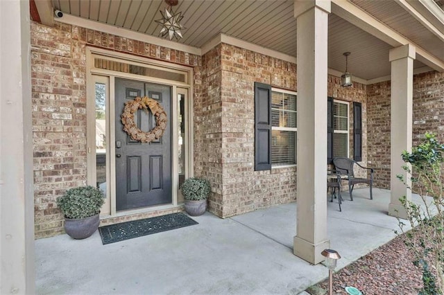 view of exterior entry featuring covered porch and brick siding
