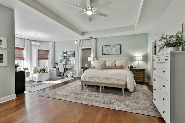 bedroom with a tray ceiling, wood finished floors, baseboards, and ceiling fan with notable chandelier