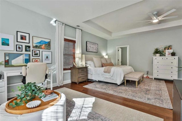 bedroom featuring baseboards, wood finished floors, visible vents, and a raised ceiling