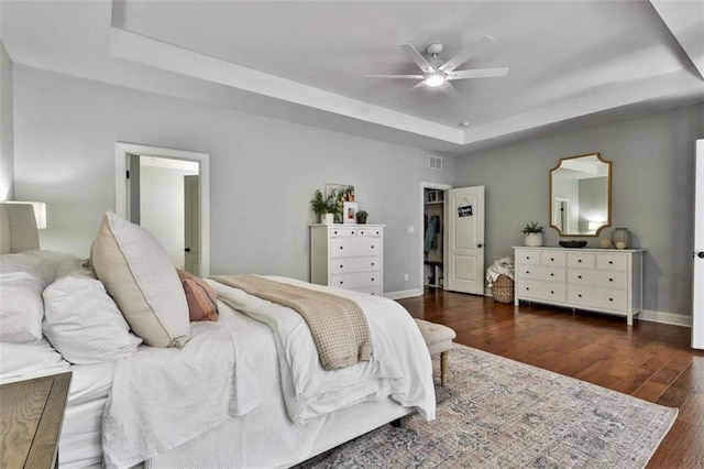 bedroom with a ceiling fan, wood finished floors, a tray ceiling, baseboards, and visible vents