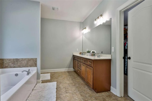 full bathroom featuring a sink, a bath, double vanity, baseboards, and stone finish floor