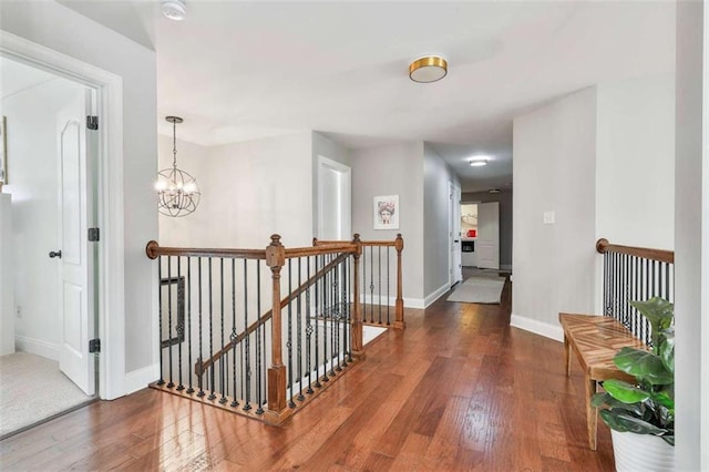 hallway with baseboards, a notable chandelier, wood finished floors, and an upstairs landing