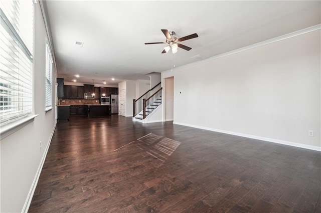 unfurnished living room with stairs, a ceiling fan, baseboards, and dark wood-style flooring