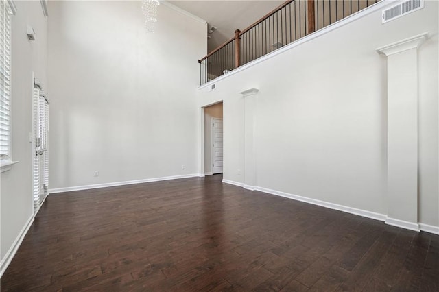 unfurnished living room with baseboards, visible vents, dark wood-style floors, and a towering ceiling
