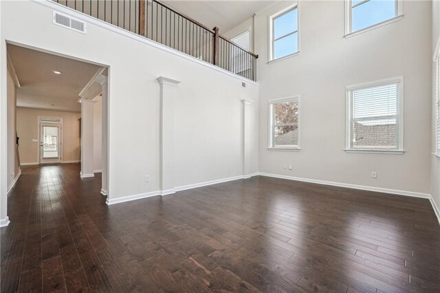 unfurnished living room with baseboards, visible vents, dark wood-type flooring, and a towering ceiling
