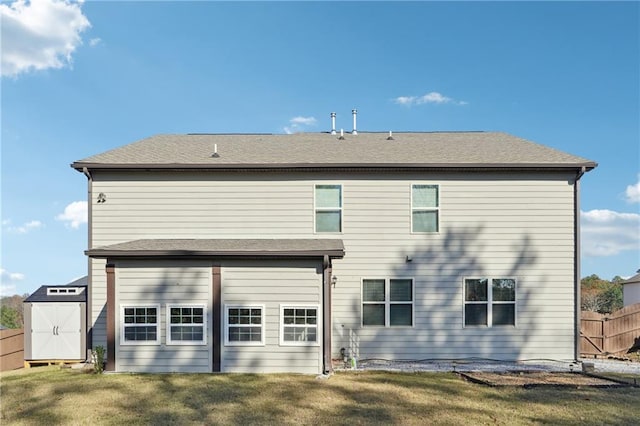 back of house with fence, a yard, a shed, an attached garage, and an outbuilding