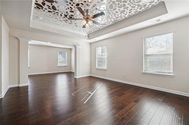 empty room with visible vents, decorative columns, baseboards, ceiling fan, and a tray ceiling