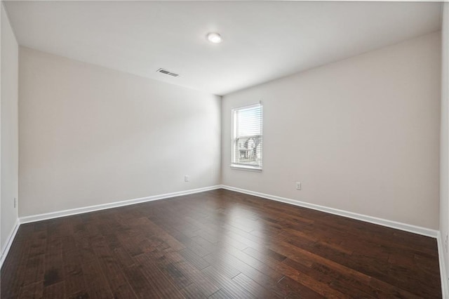 spare room featuring baseboards, visible vents, and dark wood finished floors