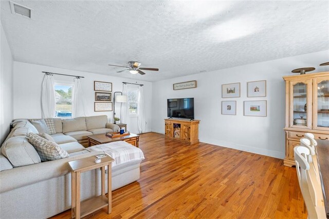 living area featuring visible vents, ceiling fan, a textured ceiling, and light wood-style floors