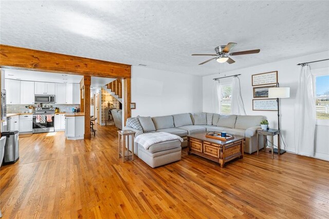 living area featuring stairs, a ceiling fan, light wood-style floors, and a textured ceiling