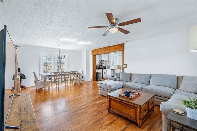 living room with a textured ceiling, light wood-style flooring, and ceiling fan with notable chandelier