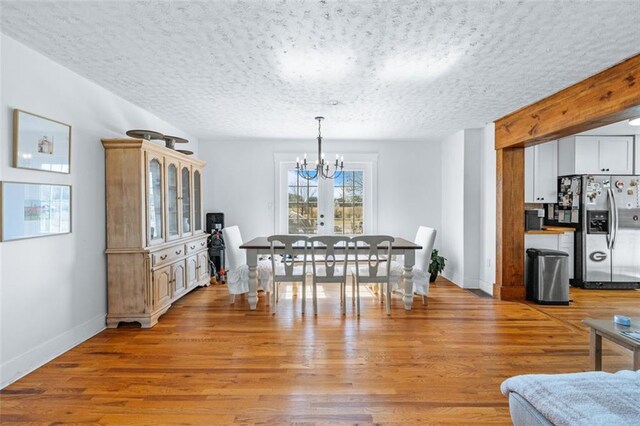 dining area featuring a chandelier, baseboards, a textured ceiling, and light wood-style flooring