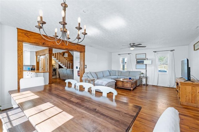 living room featuring ceiling fan with notable chandelier, stairway, wood finished floors, and a textured ceiling