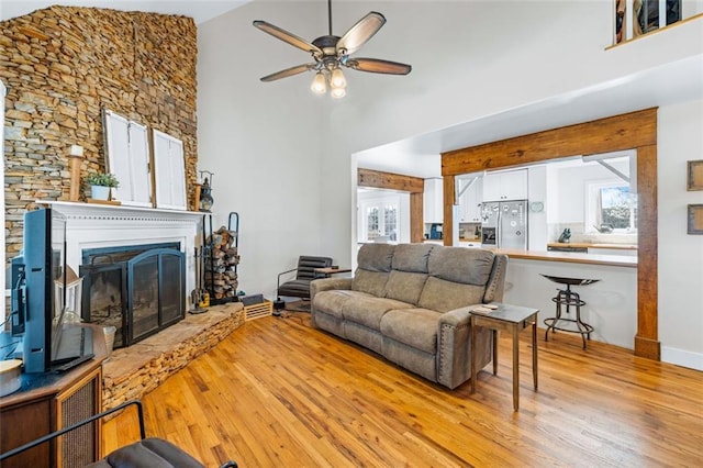 living area with a ceiling fan, wood finished floors, a towering ceiling, and a fireplace with raised hearth