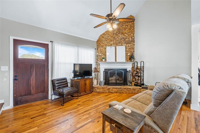 living room featuring a stone fireplace, ceiling fan, high vaulted ceiling, and light wood-style floors