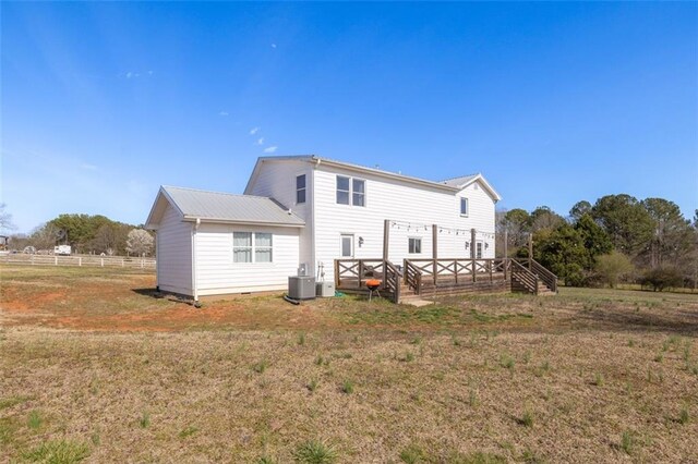 back of property with a yard, central air condition unit, metal roof, and fence