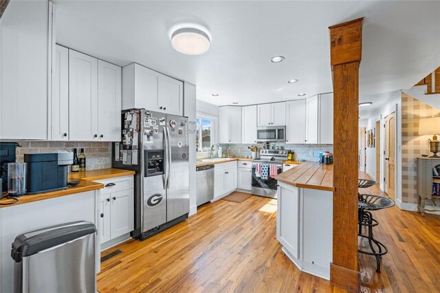 kitchen with a kitchen bar, a sink, white cabinetry, stainless steel appliances, and light wood-style floors