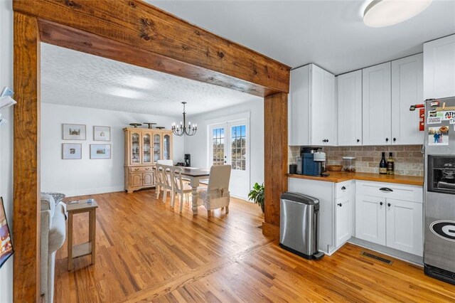 kitchen with visible vents, light wood-type flooring, decorative backsplash, white cabinets, and stainless steel fridge