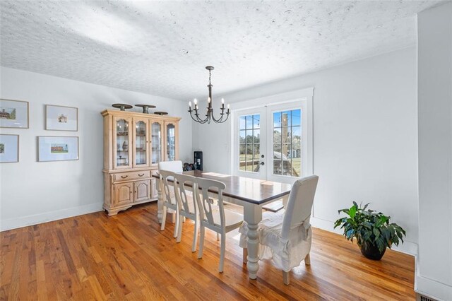 dining room featuring light wood-style flooring, a textured ceiling, french doors, an inviting chandelier, and baseboards