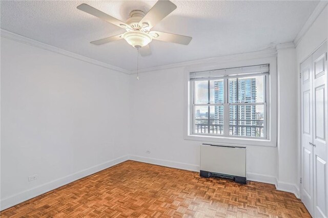 spare room featuring a textured ceiling, parquet flooring, ceiling fan, and crown molding