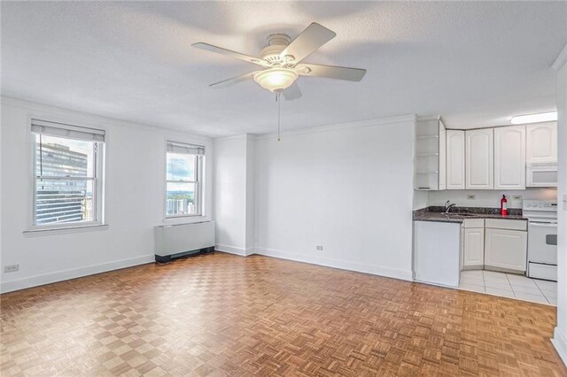 kitchen with radiator heating unit, a textured ceiling, ceiling fan, white cabinetry, and white appliances