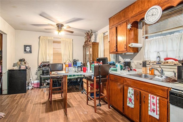 kitchen with a sink, light countertops, light wood-type flooring, brown cabinets, and dishwasher