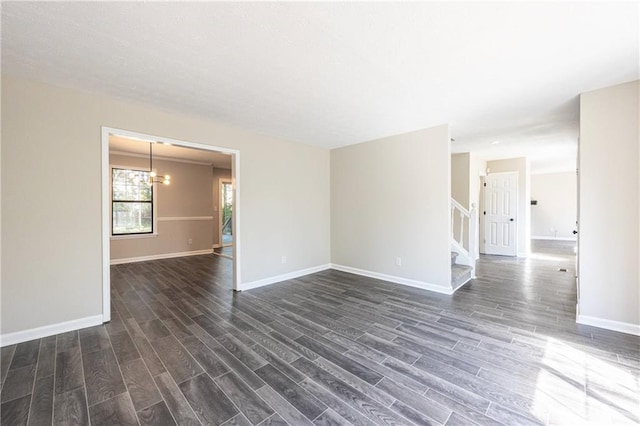 spare room featuring dark wood-style floors, an inviting chandelier, baseboards, and stairs