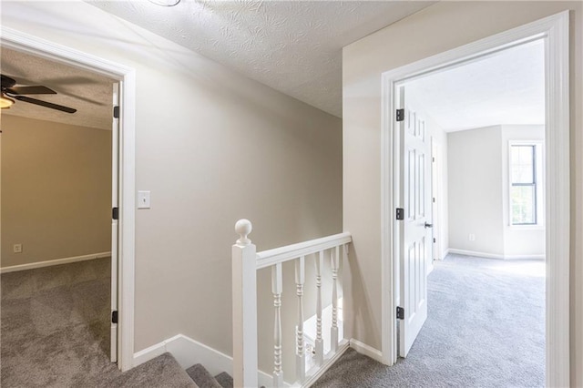 hallway featuring a textured ceiling, carpet flooring, and an upstairs landing