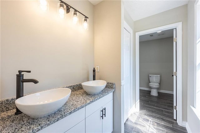 full bathroom with baseboards, a sink, toilet, and double vanity