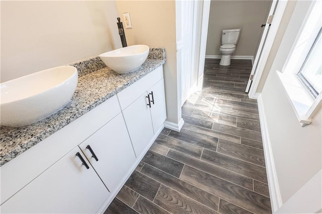 bathroom featuring wood tiled floor, a sink, toilet, and double vanity