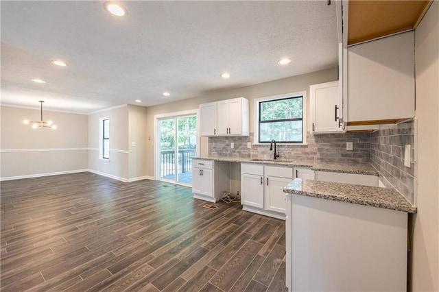 kitchen with tasteful backsplash, dark wood-type flooring, white cabinets, a sink, and light stone countertops