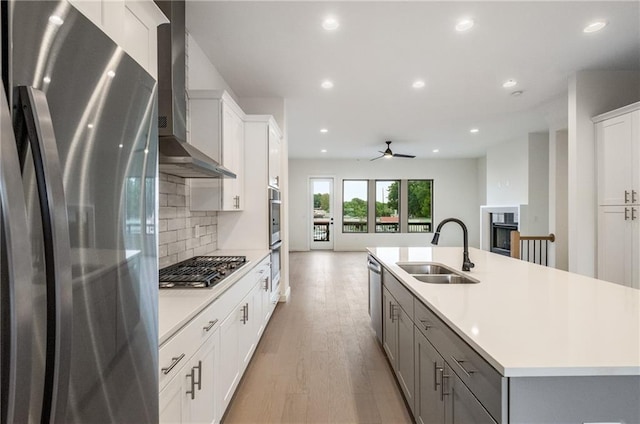 kitchen with a kitchen island with sink, wall chimney exhaust hood, white cabinetry, light hardwood / wood-style flooring, and appliances with stainless steel finishes