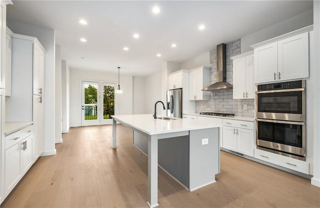 kitchen featuring pendant lighting, wall chimney range hood, stainless steel appliances, and white cabinets