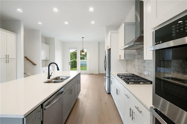 kitchen featuring hanging light fixtures, sink, wall chimney exhaust hood, white cabinetry, and appliances with stainless steel finishes