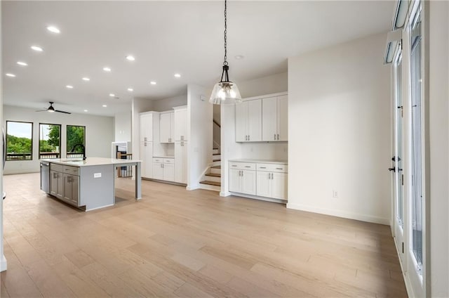 kitchen with a center island with sink, light wood-type flooring, decorative light fixtures, and white cabinetry